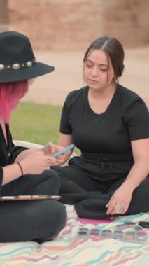 Siyah elbiseli iki arkadaş yerde oturup etkileşime girerken, biri cep telefonunda mesaj atıyor. Yavaş çekim, döndürme - Dikey 1080 video