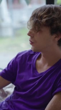 Sarışın bir çocuk, FullHD dikey video içerken cep telefonuna bakar.