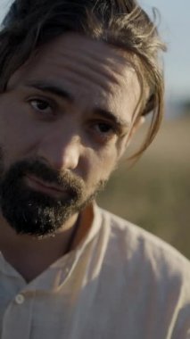 Gün batımında gitar çalan ve nehir kenarında şarkı söyleyen sakallı bir İspanyol adam.