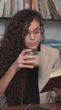 Faslı genç bir kadın ilginç bir kitap okurken kahve içiyor. - Yakın plan - Dikey
