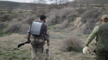 Bir tavşan ve bir dağ gelinciği ile yürüyen tanınmayan iki avcı - 4K Yatay video
