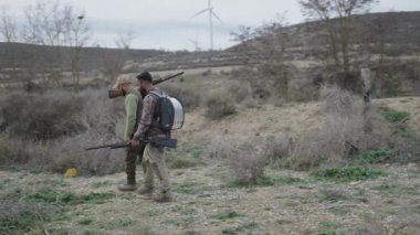 Silahlı iki avcı yürüyor ve selam veriyor - 4K Yatay video