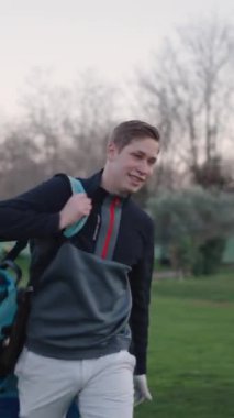 Genç bir golfçü golf ekipmanlarını taşırken gülümsüyor.