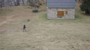 Kafkasyalı, şapkalı ve sırt çantalı olgun bir kadın her gün köpeğiyle birlikte dağdan geçiyor. 4K yatay video.