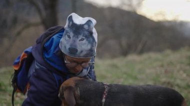 Ağır çekim beyaz kadın, doğada agacahda şapkalı Alman çoban köpeğini okşayan - 4K yatay video.