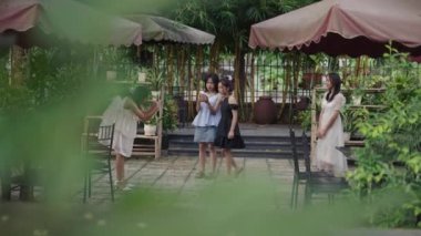 Yavaş çekim dört Asyalı genç kız şık yaz kıyafetleri içinde barın terasında mutlu ve memnun fotoğraflar çekiyorlar - 4K Yatay Video