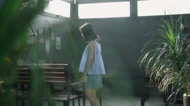 Ağır çekim genç Asyalı kız elinde akıllı telefonuyla terasta içki listesini kontrol ediyor. 4K yatay video.