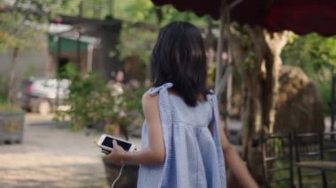 Ağır çekimde, elinde akıllı telefonuyla bahçede arkadaşlarıyla fotoğraf çeken ve 4K Yatay Video 'nun keyfini çıkaran Asyalı genç bir kız.