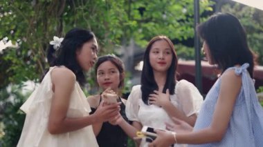 Orta ölçekli ağır çekim. Dört zarif Asyalı genç kız yazın akıllı telefonuyla fotoğraf çekiyor. 4K Yatay Video.