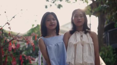 Ağır çekimde yan yana iki Asyalı genç kız kameraya gülümsüyor yazın bahçede güneşin altında mutlu mesut gülümsüyorlar - 4K Yatay video