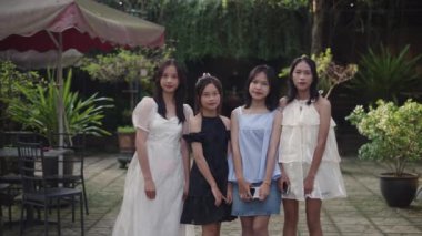 Yavaş çekim zoom dört genç Asyalı kız yaz elbiseleri ve elinde akıllı telefonla kameraya yan yana gülümseyerek poz veriyor - 4K yatay video