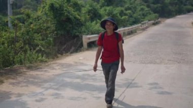 Mutlu ve memnun Vietnamlı bir sığır çobanı sigara içerken yolda inekleri güderken kameraya bakıyor - 4K Yatay Video