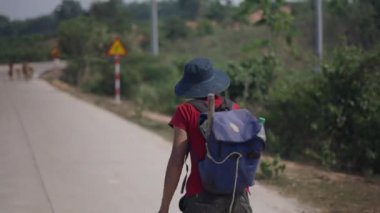 Sırt çantası ve sopalı Vietnamlı Asyalı çoban yolda sürtünürken sigara içiyor - 4K Yatay Video