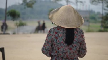 Sırtında çiçek desenli elbisesi ve Vietnam 'da turistleri gezdiren fillere bakan şapkalı olgun bir kadın. 4K Yatay video.