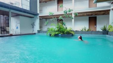 Ağır çekimde tek başına yüzen Asyalı kız yağmurlu bir günde Bangkok Tayland 'da bir havuzda - 4K Yatay Video