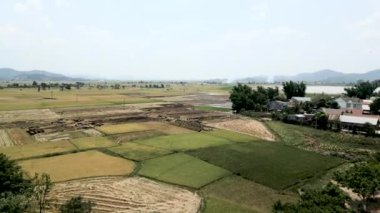 Vietnam 'da göl kenarındaki kırsal bir alanda ve doğanın ortasındaki dağlarda ekin tarlaları üzerinde havadan panoramik dron görüntüsü - 4K Yatay video