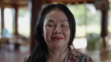 Asyalı Vietnamlı bir kadının portresi. Uzun saçlı ve çiçekli elbisesi boyalı dudaklarıyla kameraya gülümsüyor. 4K yatay video.