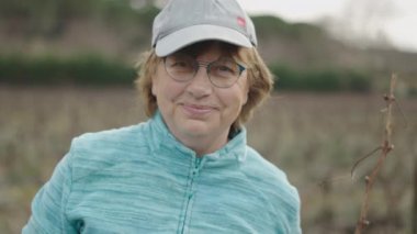 Üzüm bağında kameraya gülümseyen yaşlı beyaz bir çiftçinin yüzünü kapatın. 4K Yatay Video.