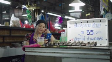 Asyalı olgun bayan balık dükkanında oturduğu akıllı telefon ekranını kontrol ediyor. 4K yatay video.