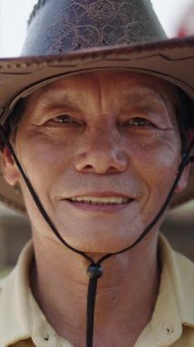 Kameraya bakıp gülümseyen yetişkin bir Vietnamlı adamın portresi şapka ve gömlek giyiyor.