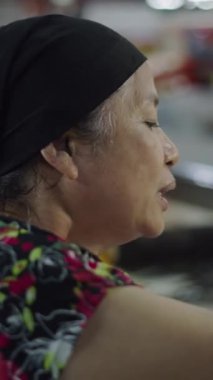 Elinde faturalar olan bir balıkçıdan gelen Asyalı olgun bir kadın yerel bir markette bir başkasına ödeme yapıyor.