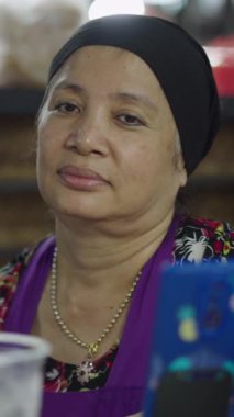 Yetişkin bir Asyalı kadının portresi yerel bir markette servis edilmeyi beklerken kameraya bakıyor.