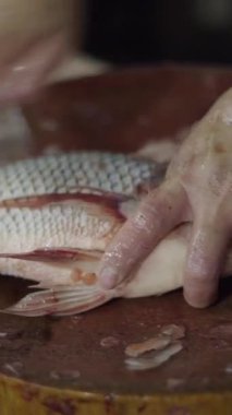 Balık satıcısı yerel bir pazarda büyük bir bıçakla taze balığın derisini temizliyor ve yüzüyor.