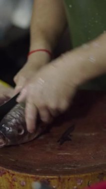 Balıkçı yerel bir markette büyük bir bıçakla yuvarlak bir ahşap üzerinde çiğ balık temizliyor ve kesiyor.