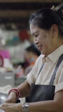 Asyalı olgun kadın mutlu ve gülümseyen tavuk kesiyor ve yerel bir pazarda satılık bıçakla tavuk hazırlıyor.
