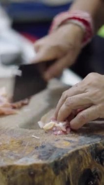 Asyalı kasap kadın büyük, sert bir ahşap üzerinde büyük bir bıçakla tavuk etini keser ve hazırlar.