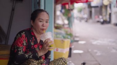 Olgun Asyalı balıkçı Vietnam 'da Ho Chi Minh City caddesinde bir markette müşteriyle konuşurken plastik bardaktan su içer.
