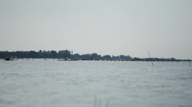 Büyük şapkalı bir balıkçı, bulutlu ve rüzgarlı bir günde, Tritri 'deki büyük balık çiftliğinde çalışır.