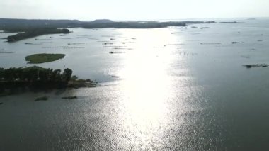 Güneşin rüzgarlı bir günde sularına yansıdığı Tri An Gölü 'nün panoramik hava manzarası - 4K Yatay