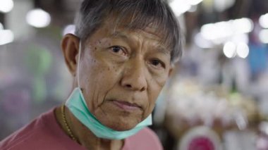 Boynunda yüz maskesi olan olgun bir adamın portresi Bangkok Tayland 'da bir markette kamera dükkanına bakıyor - 4K Yatay Video