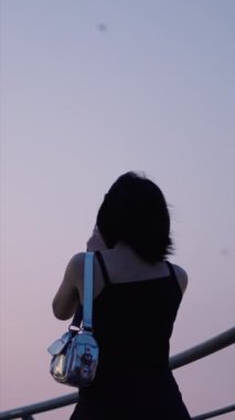 Sırtında gümüş çantalı bir kız ho chi minh şehrinde hayret verici bir gökyüzünün fotoğrafını çekiyor HCMC Saygon Vietnam FullHD Dikey