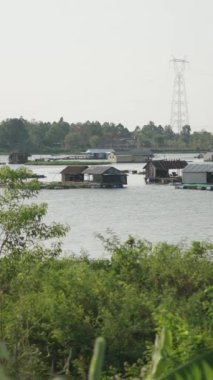 Suyun ortasında yüzen evler balık çiftliklerinin yanında Vietnam Gölü 'nün ortasında palmiye ağaçları ve bitkilerle çevrili FullHD dikey