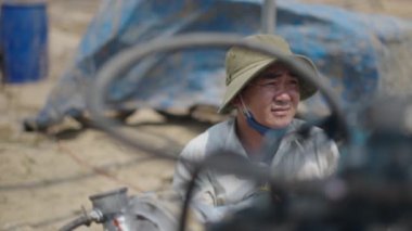 Yavaş çekim Vietnamlı tamirci büyük şapkalı bir teknenin motorunu tamir ediyor - 4K Yatay