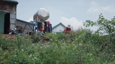 Büyük şapkalı genç Vietnamlı kadın elbiselerini bir musluğun yanında yıkıyor - 4K Yatay