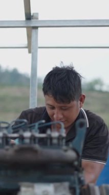 Genç Vietnamlı tamirci eski bir motoru tamir ederken mutlu bir şekilde gülümsüyor - FullHD dikey
