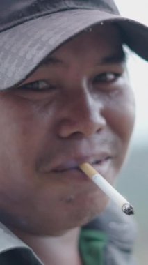Kafasında bir şapka ve ağzında bir sigarayla kameraya bakan Asyalı genç bir Vietnamlının portresi.