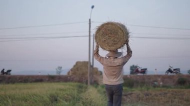 Sırtında büyük yuvarlak bir saman balyasıyla Asyalı çiftçi Vietnam 'da kameraya gülümserken - 4K Yatay