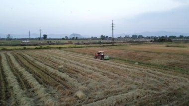 İnsansız hava aracı, traktörün samanı sıkıştırıp Vietnam 'da büyük balyalara dönüştürdüğü tarlaların üzerinde uçuyor. 4K Yatay