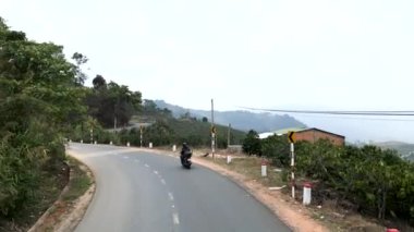 Vietnam 'da ağaçlar ve dağ bitkileri arasındaki virajlı yolda yavaş giden motosiklet - 4K Yatay