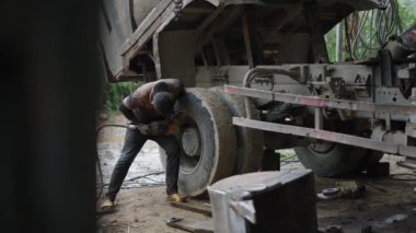 Ağzında sigara ve şapkası olan genç bir tamirci Vietnam 'da bir kamyon tekerleğinin cıvatalarını gevşetiyor - 4K Yatay