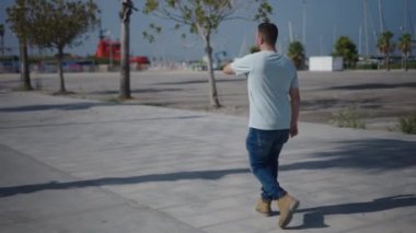 Palmiye ağaçları arasındaki çimento geçidi boyunca kameraya doğru yürüyen beyaz çocuk akıllı telefonuyla bir ses notu gönderiyor. 4K yatay video.