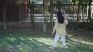 Bir esmer ve bir sarışın solda yürüyorlar ve çimlerin üzerinde çıplak ayakla sohbet ediyorlar - 4K Yatay