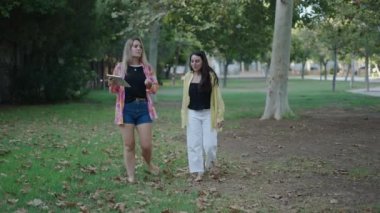 Genç sarışın beyaz kız çimenlerin üzerinde kameraya doğru yürüyor ve tabletle bir video görüşmesi yaparken gülümsüyor - 4K Yatay