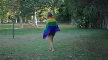 Bir esmer ve bir sarışın çıplak ayakla kameraya doğru yürüyorlar ve aralarında bir LGBT bayrağı sallıyorlar - 4K Yatay