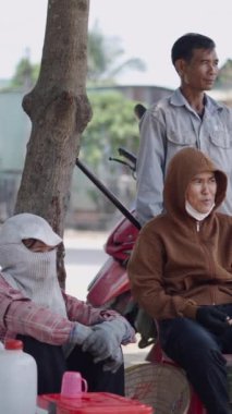 Üç Asyalı, Vietnam 'da yolun kenarındaki bir ağacın altında sessizce dinlenip sohbet ediyor.