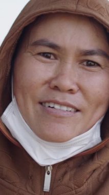 Boynunda yüz maskesi olan Asyalı genç bir kadının V şeklinde parmaklarıyla kameraya el sallaması.